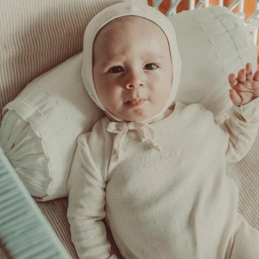 Baby wearing the Lovely Littles Oatmilk Pointelle romper and bonnet